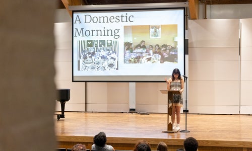A student at a podium on stage making a presentation, photographed from the back of an auditorium.