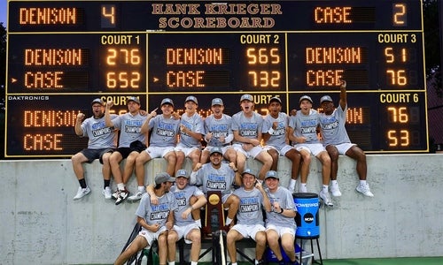 The Men's Tennis team with their trophy in front of the final scoreboard.